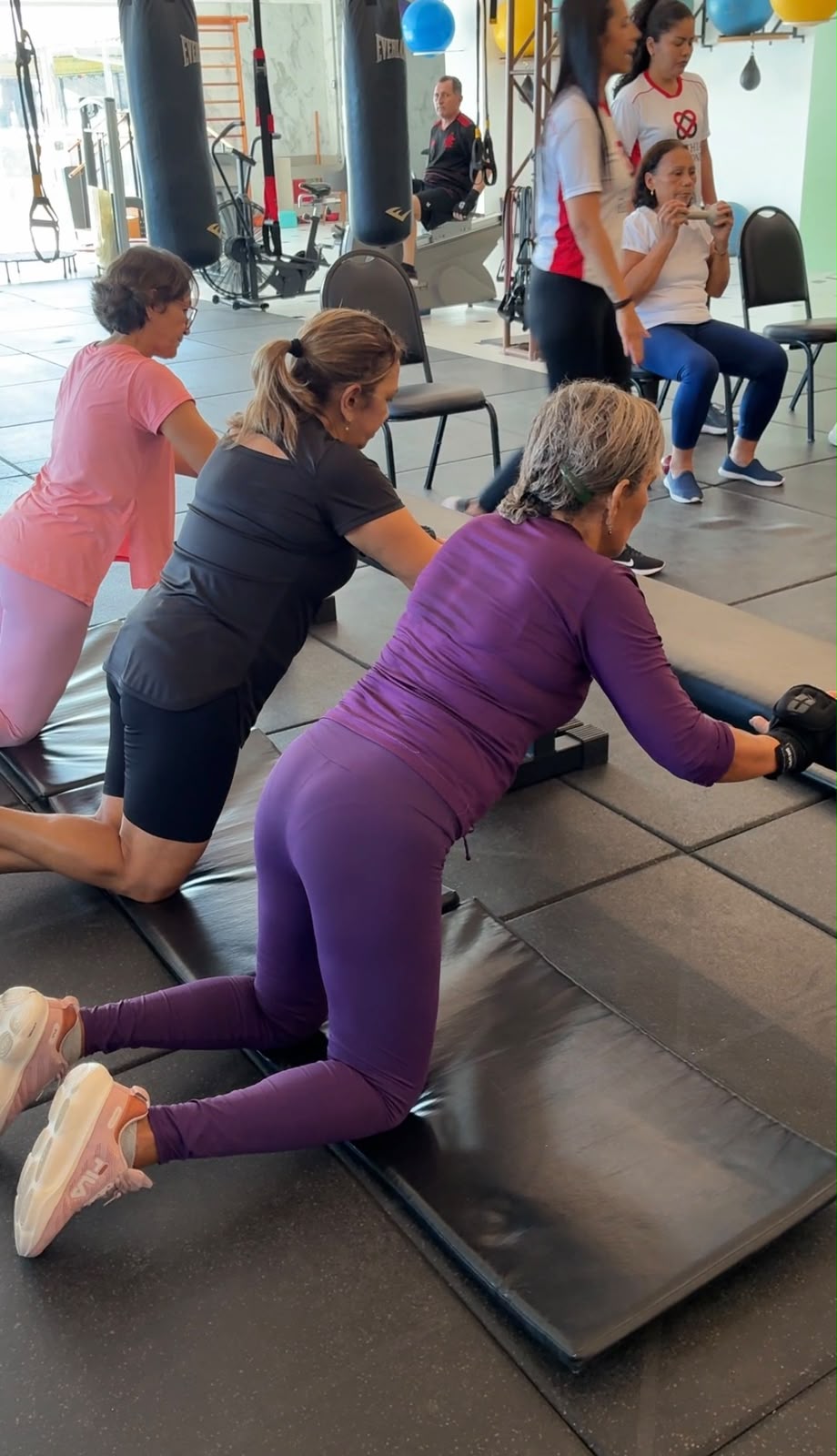 Pacientes idosas realizam exercícios de alongamento no chão sobre colchonetes.