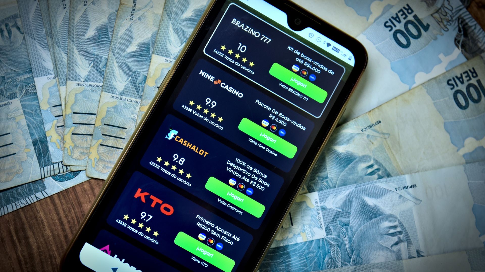 celular com tela aberta em app de bets em cima de uma mesa cheia de notas de dinheiro