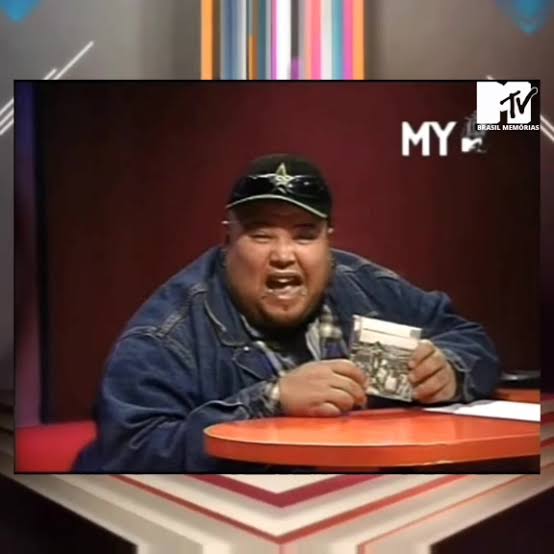 João Gordo está apoiado em uma mesa durante seu programa na MTV