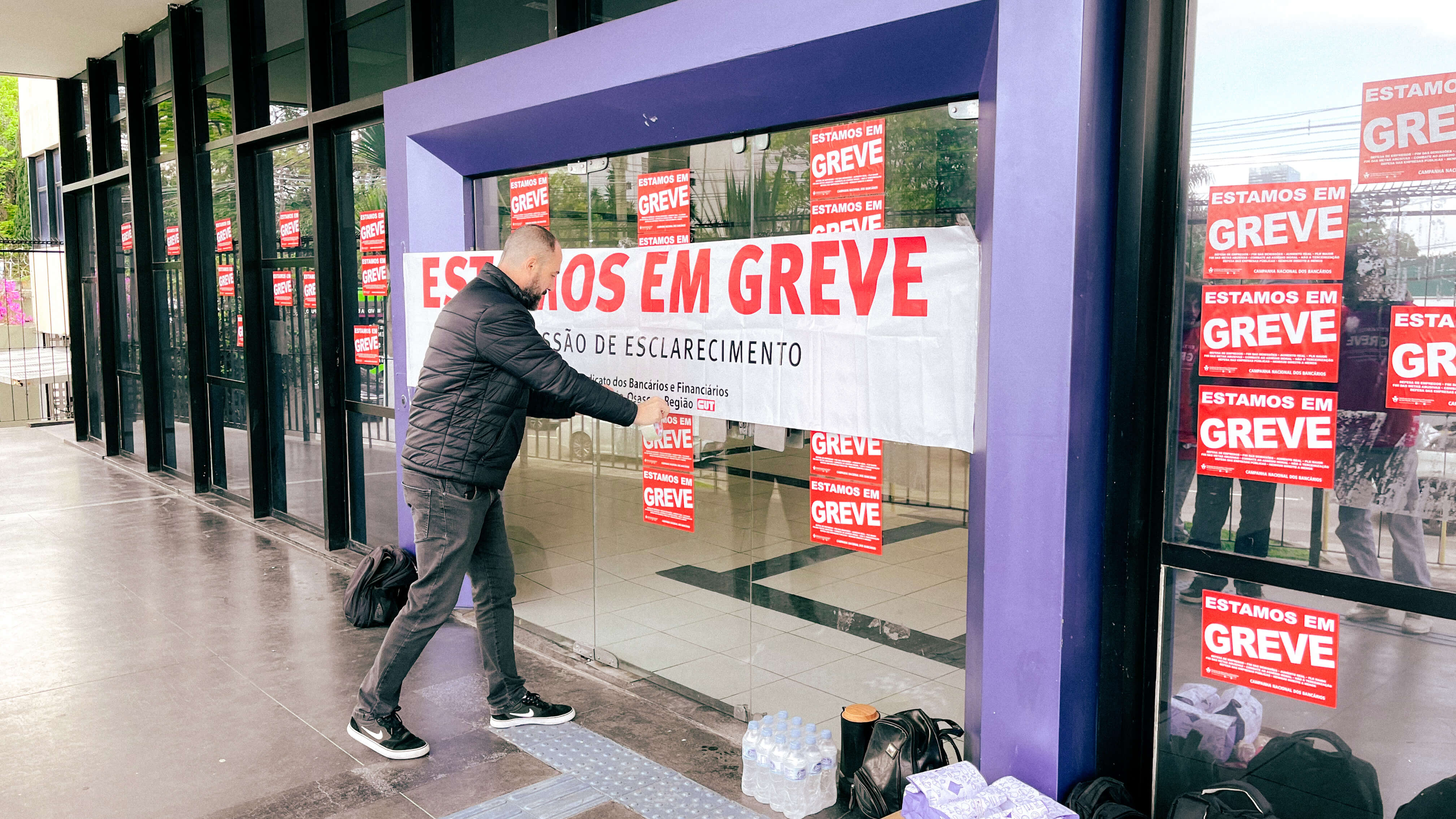 Bancário cola adesivos de "greve" em frente à fachada de agência da Caixa na zona sul de SP