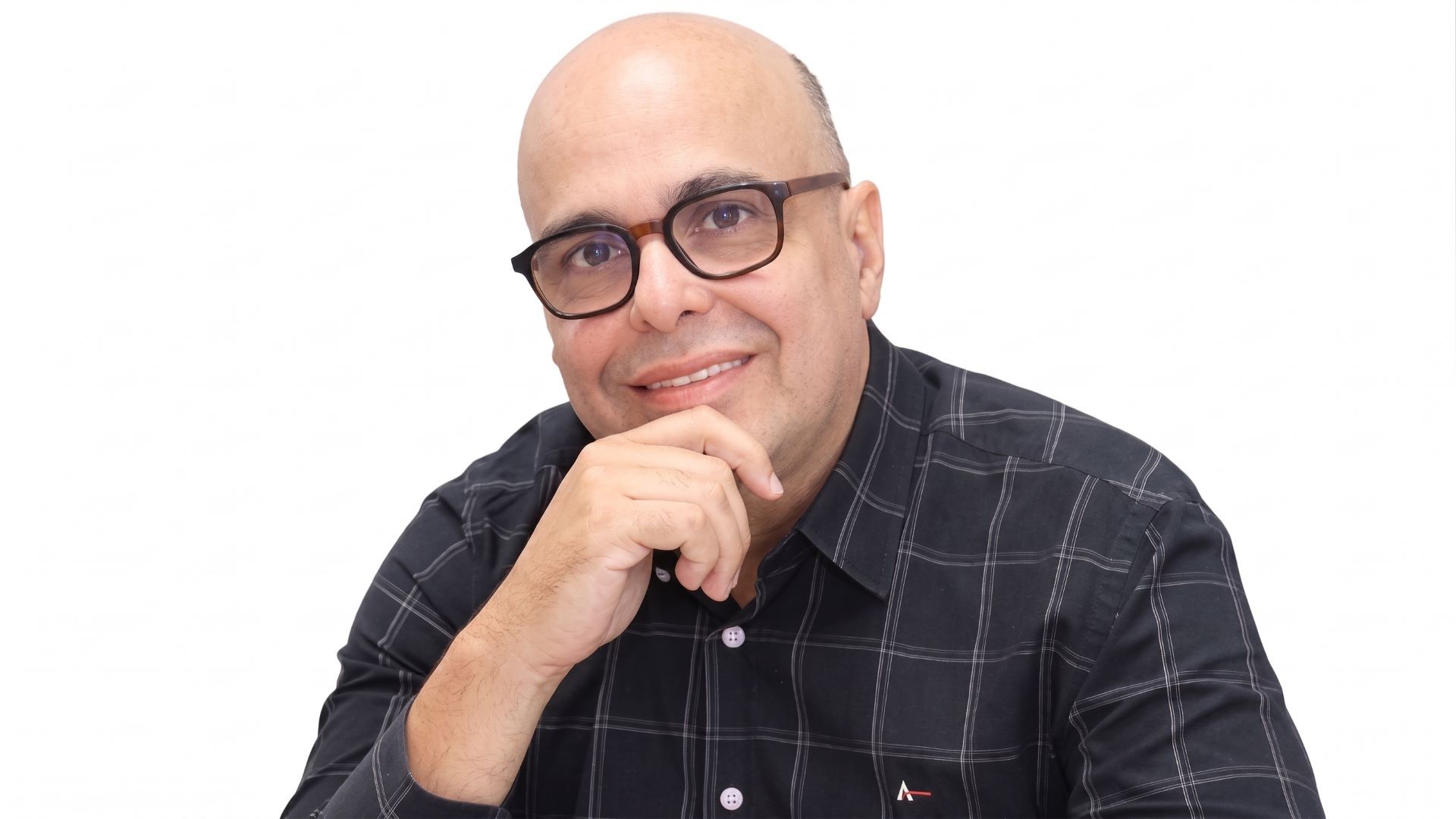 De óculos e com a mão direita sobre o queixo, Nelson Nogueira sorri para a câmera
