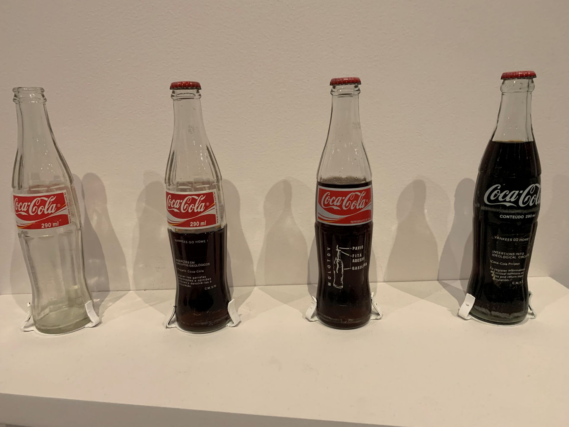 Quatro garrafas de Coca-Cola, uma do lado do outro, com intervenções