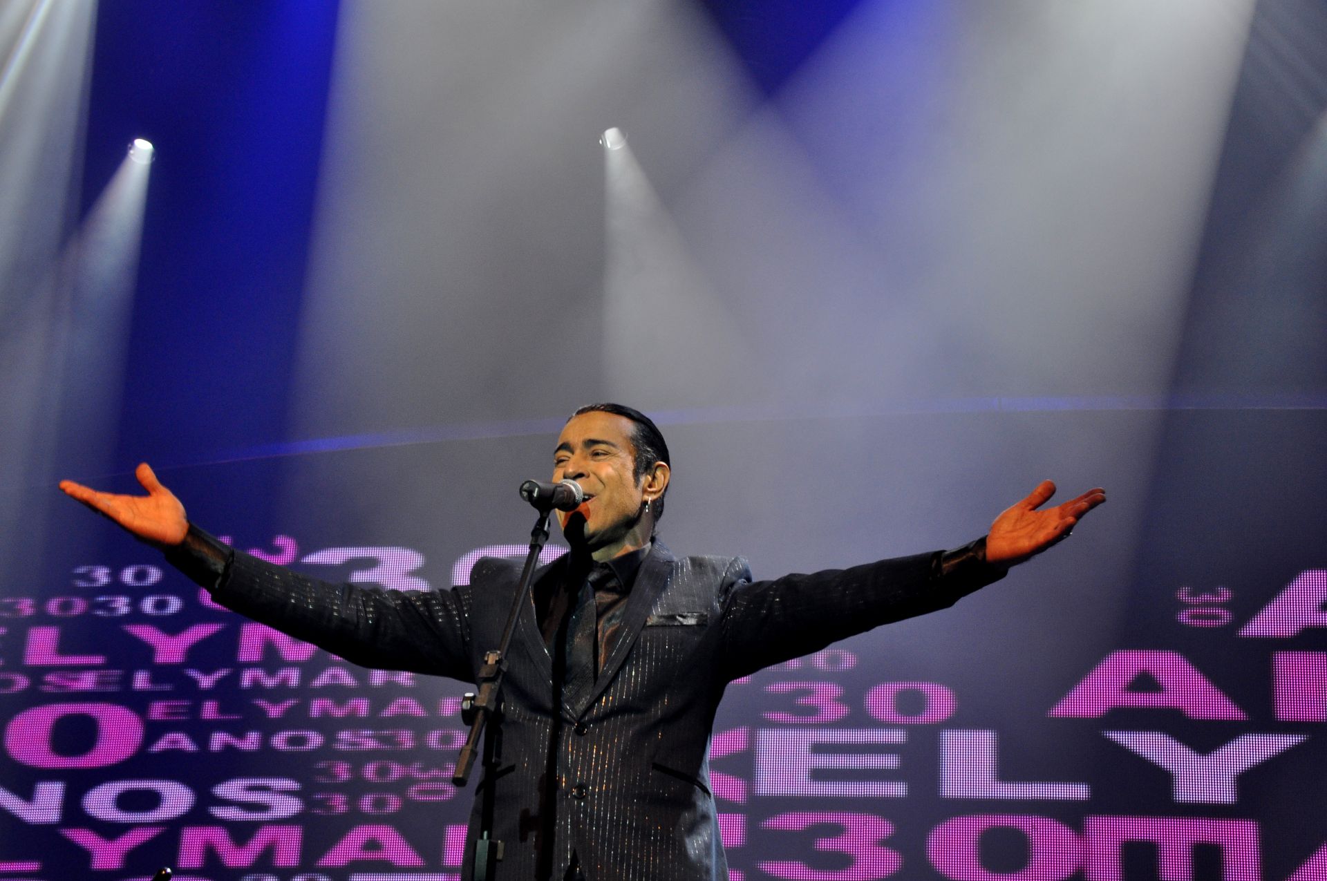 Elymar Santos está em cima do palco, com os braços abertos, cantando
