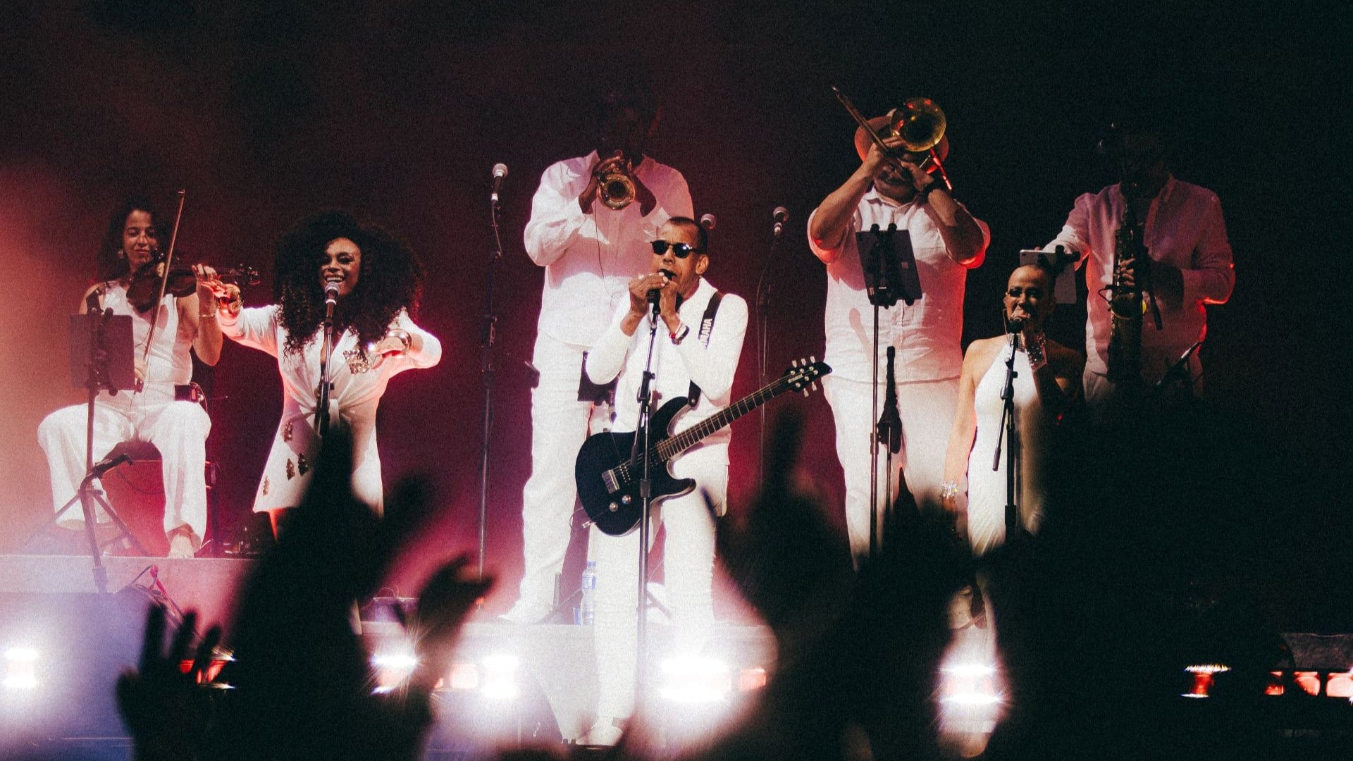 Jorge Ben Jor está cercado pelos músicos de sua banda, todos vestidos de branco