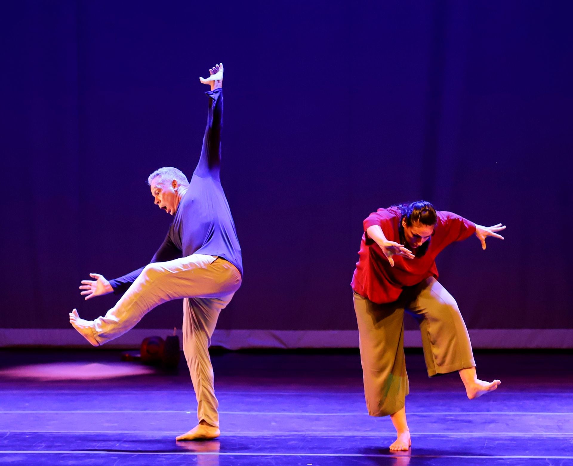 Os dois bailarinos estão dançando em cima da palco, ele com os braços para o ar e ela curvada