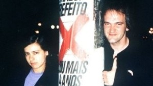 Renata de Almeida e Quentin Tarantino estão encostados em um poste em SP