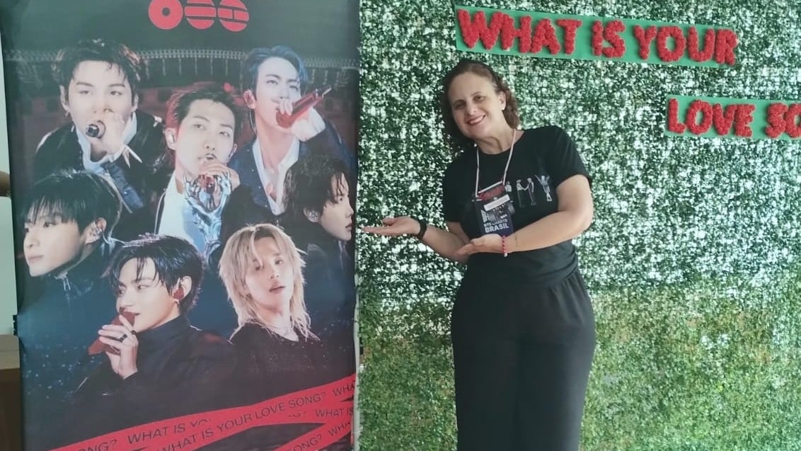 Vivan está de preto e mostrando um pôster do BTS